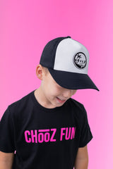 Young boy wearing a CHooZ FUN black and white curved brim youth hat, standing against a pink background