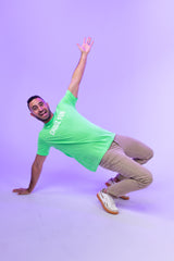 Man wearing the FUN Mark Tee in Neon Green holding a breakdance move on a purple backdrop. High-energy gear for all-out fun.