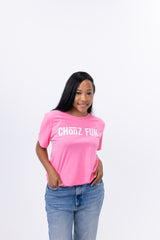 Woman standing in neon pink Fun Mark tee with hands in jeans pockets, white background. Simple stance, bold vibe.